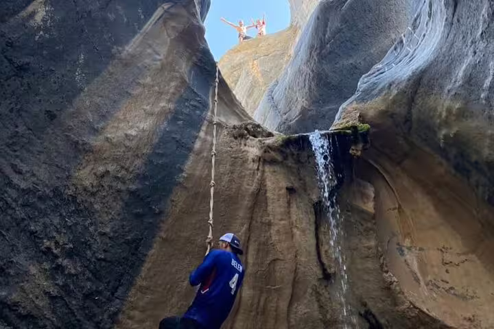 Participant climbing a rope beside a waterfall in a scenic Wadi Dham canyon.