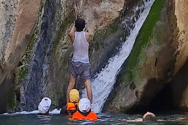 Adventurers climbing waterfall in Wadi Dham, showcasing thrilling water activities on a private full-day tour.