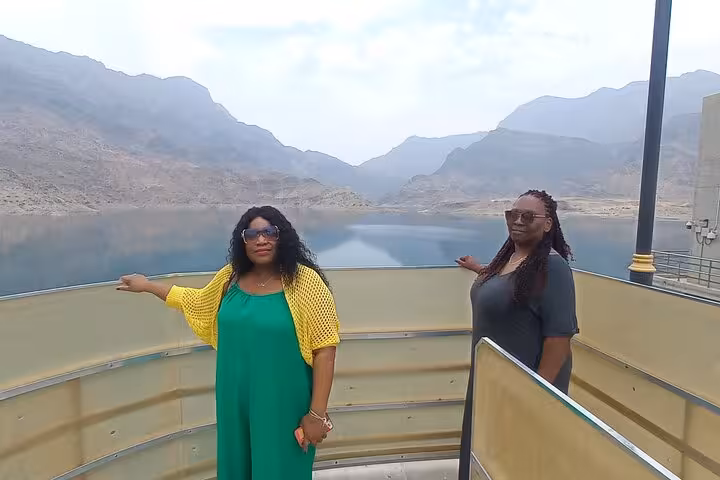 Two women enjoy panoramic mountain and lake views from a scenic lookout on a Wadi Shab and Bimmah Sinkhole day trip