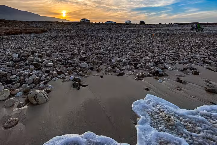 Rocky Oman coastline at sunset with parked tour vehicles, visited on a Wadi Shab and Bimmah Sinkhole day trip from Muscat