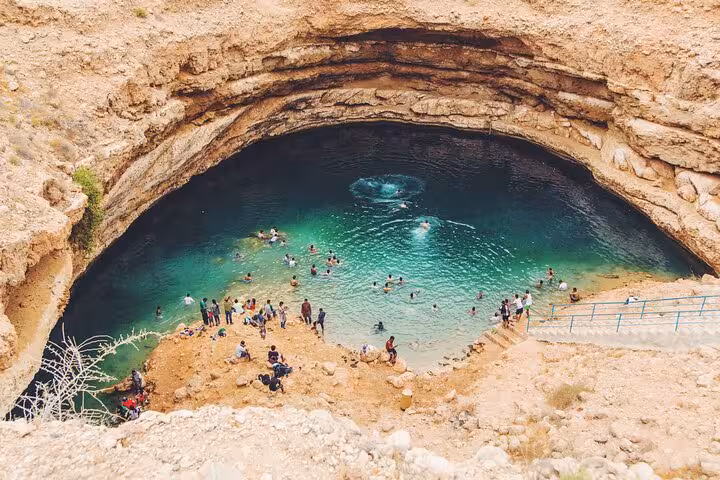 Travelers swim in the turquoise waters of Bimmah Sinkhole, a highlight of the Wadi Shab day trip from Muscat in Oman