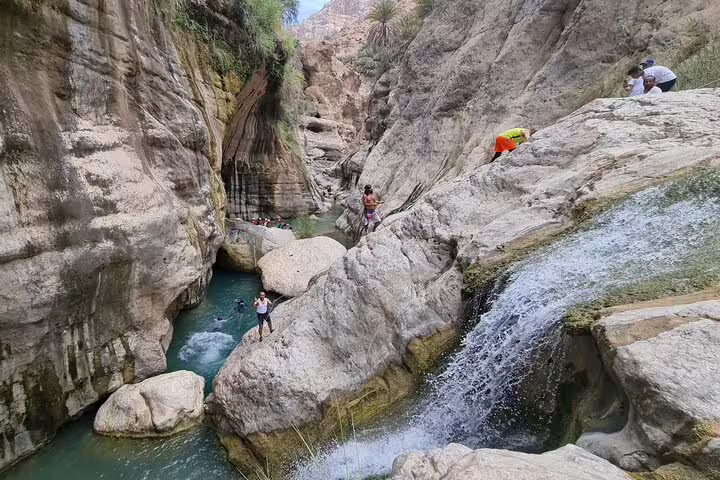 Adventurers explore the rocky terrain and turquoise waters of Wadi Tiwi on a private tour from Muscat.