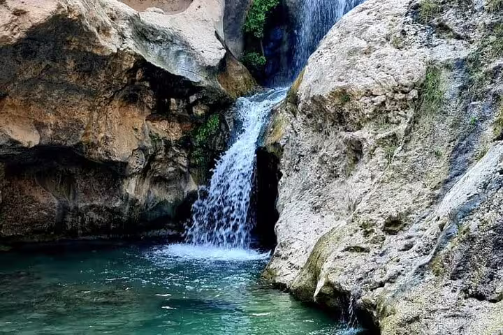 Cascading waterfall flowing into a serene pool at Wadi Tiwi, showcasing the natural beauty of Oman's landscapes.
