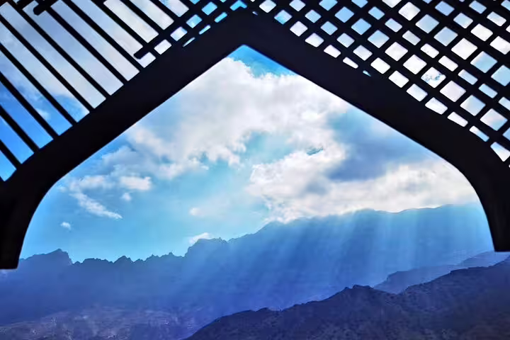Sunlight streaming through clouds over Wakan's dramatic mountain landscape framed by a traditional arch.