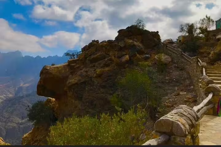 Stone pathway leading to a rocky outcrop with panoramic views of Wakan's majestic mountains under a blue sky.