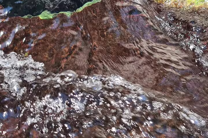 Crystal-clear water flows over vibrant rocks in Wakan, a highlight of the 2 Days 1 Night Wakan Private Tour.