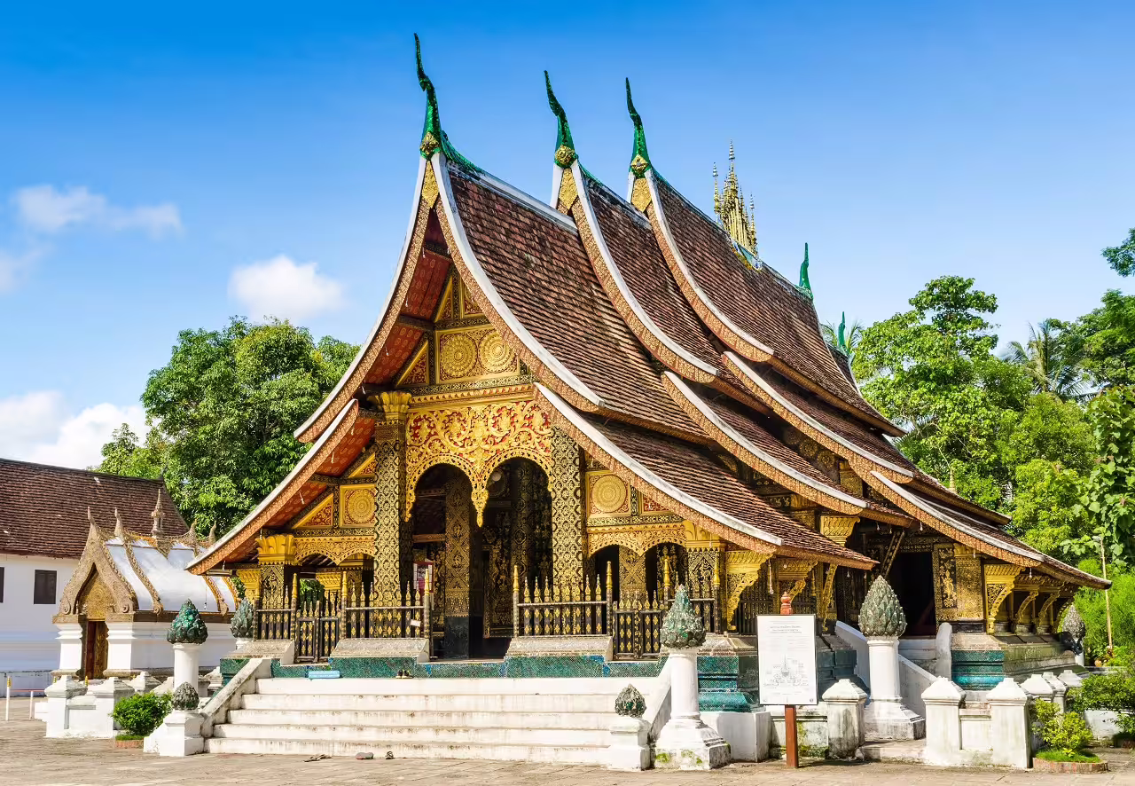 The ornate Wat Xieng Thong temple in Luang Prabang, Laos, displays intricate traditional architecture under a clear sky.