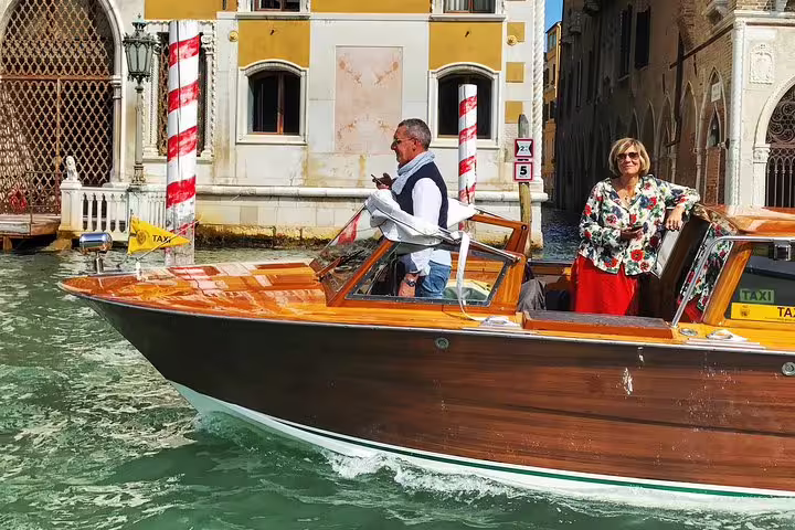 Elegant water taxi cruising along Venice's canal near historic buildings on a sunny day.