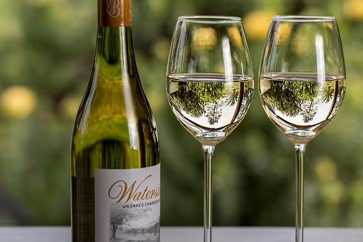 Bottle of Waterside Unoaked Chardonnay with two wine glasses against a lush vineyard backdrop.