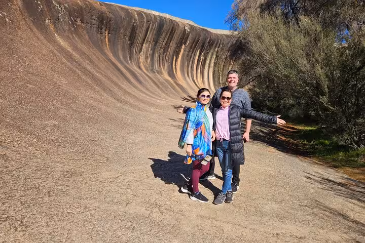 Tourists posing at the iconic Wave Rock, showcasing its unique curved rock formation on a sunny day tour in Australia.