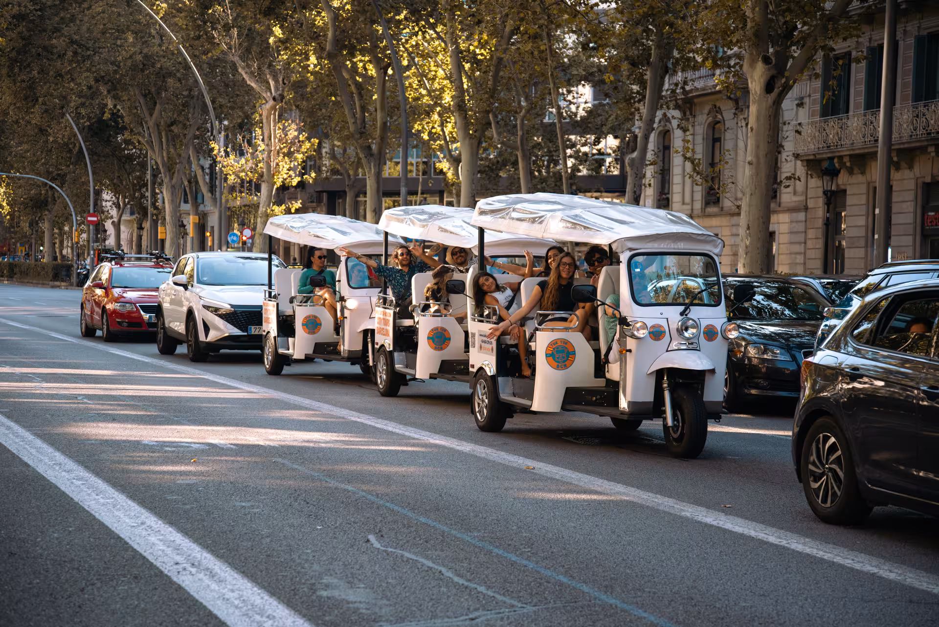 Convoy of tuk tuks with tourists cruising a tree-lined avenue on the Welcome Tour Barcelona city highlights tour