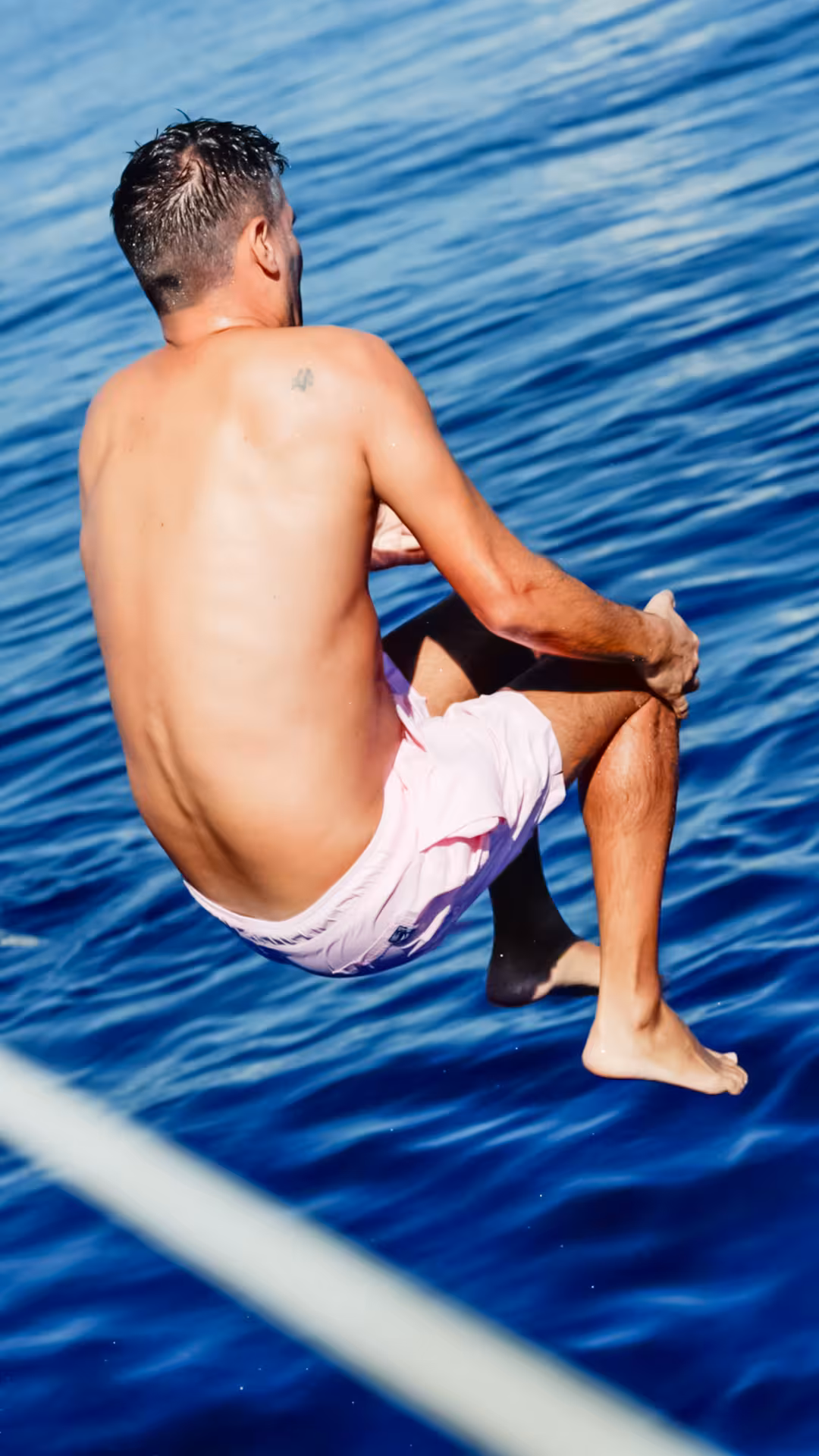 Guest jumps into clear Mediterranean water from a catamaran, refreshing sea breeze swim on wellness sailing tour