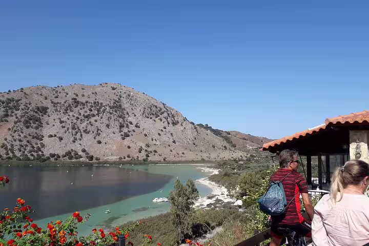 Tourists enjoying the scenic view of Kournas Lake and surrounding mountains on a sunny day in West Crete's picturesque landscape.