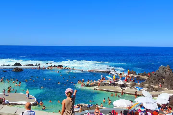 Crowded natural swimming pools by the ocean with people enjoying the sunny weather and vibrant blue waters.