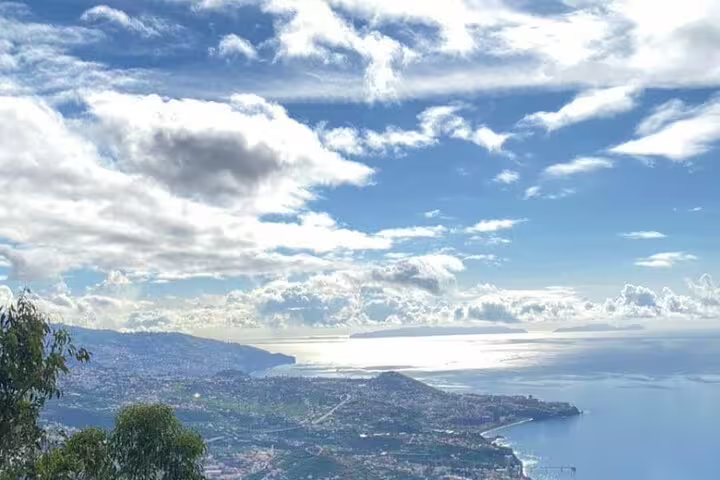 Breathtaking panoramic view over lush landscapes and shimmering ocean under a vast, cloudy sky at West Tour site.