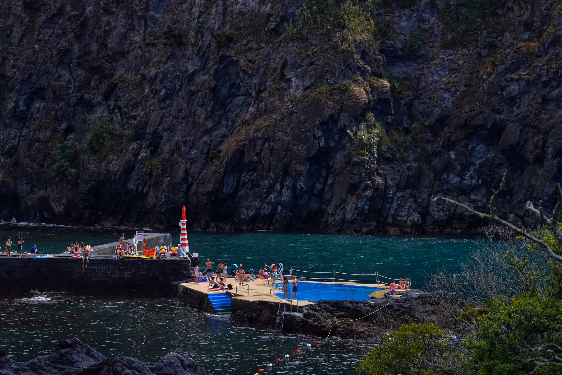 Travelers relaxing by natural sea pool and swimming area in Caloura harbor cliffs on Azores coastal day tour