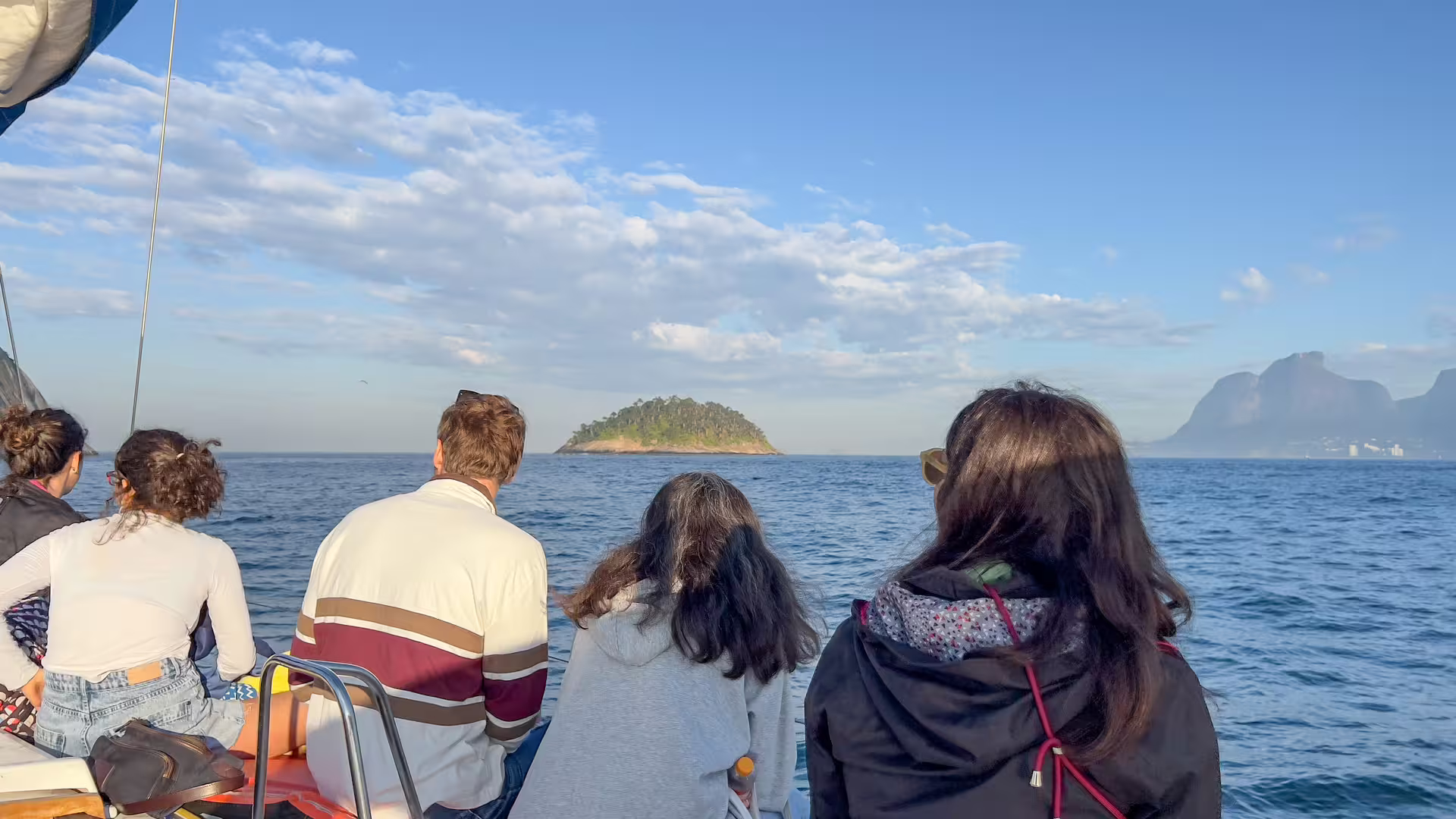 Passengers on boat scanning horizon near islands and coastline on whale watching expedition in calm blue sea