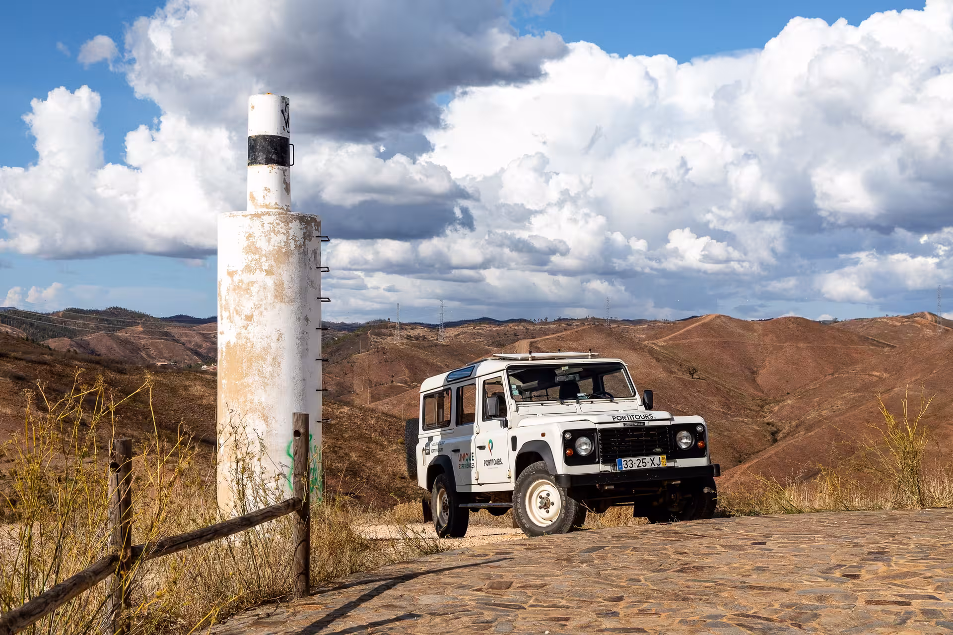 White 4x4 jeep parked at a scenic Algarve viewpoint with rolling hills and dramatic clouds on a Portugal jeep safari tour