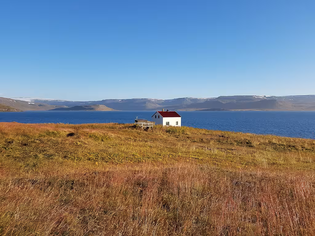 Remote white cabin by Arctic fjord under clear summer sky, landscape on Midnight Sun & Arctic Foxes tour