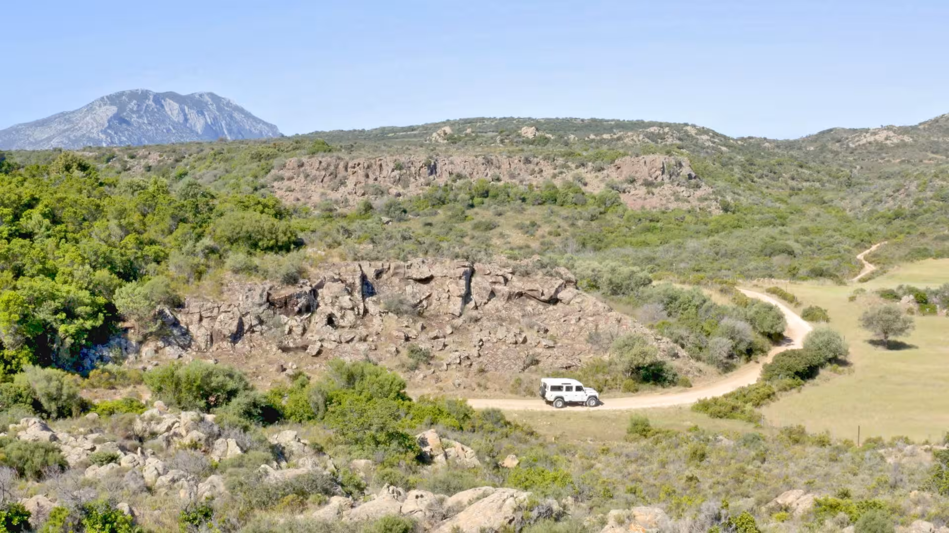 White jeep navigating scenic rocky landscapes with distant mountains on the Capo Comino private tour from Orosei.