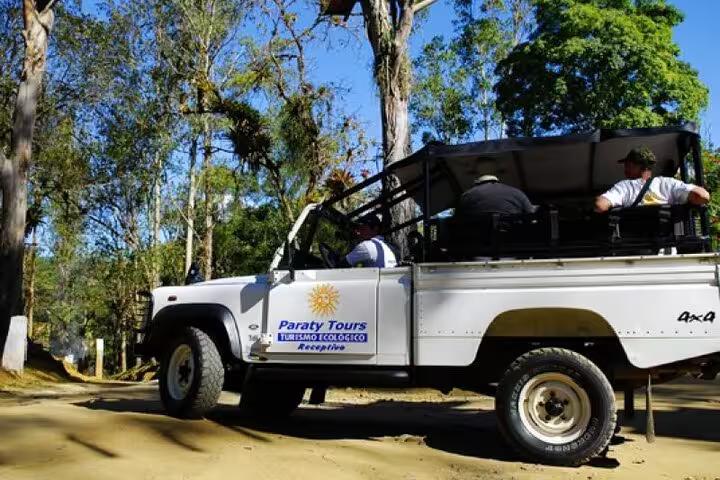 White jeep with Paraty Tours logo navigating lush forest trails on a private tour, offering an eco-friendly adventure.