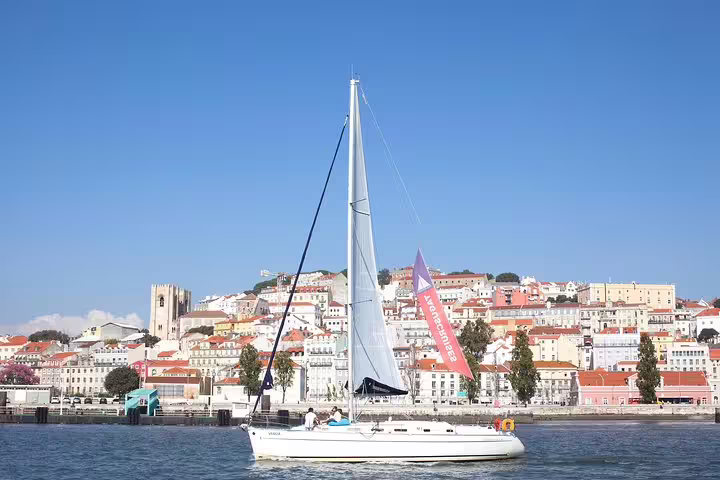 White sailboat cruising the Tagus River, showcasing Lisbon's colorful architecture and vibrant cityscape.