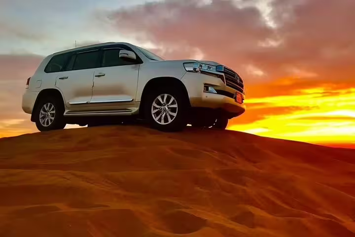 A white SUV stands majestically on a sand dune against a vibrant sunrise in the Dubai desert safari tour.