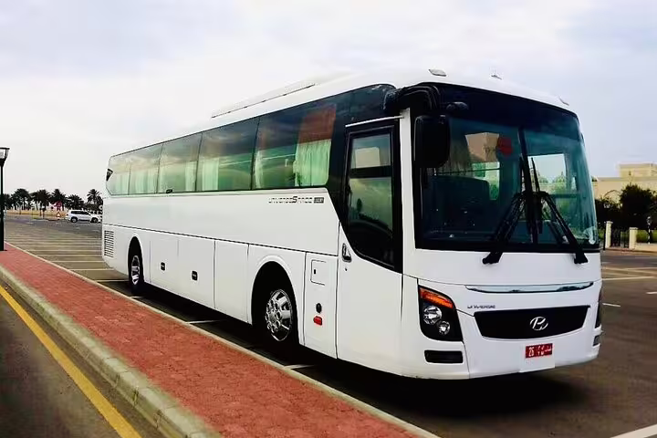 Modern white tour bus parked in Muscat, prepared for scenic journey to Wadi Shab with ample seating.