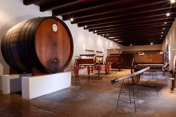 Interior of a wine cellar showcasing large barrels and vintage carts, part of the wine tasting experience.