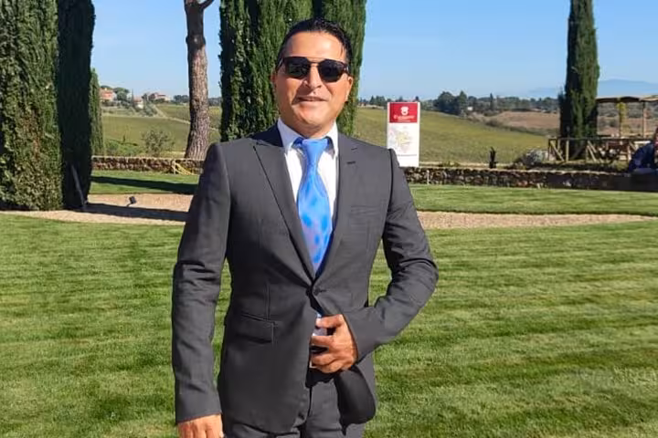 Man in formal attire stands confidently in a lush vineyard, representing a wine education course in Rome.