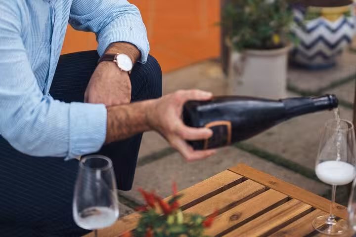 Man pours sparkling wine into glasses on a wooden table during a semi-private wine pairing in Sorrento.