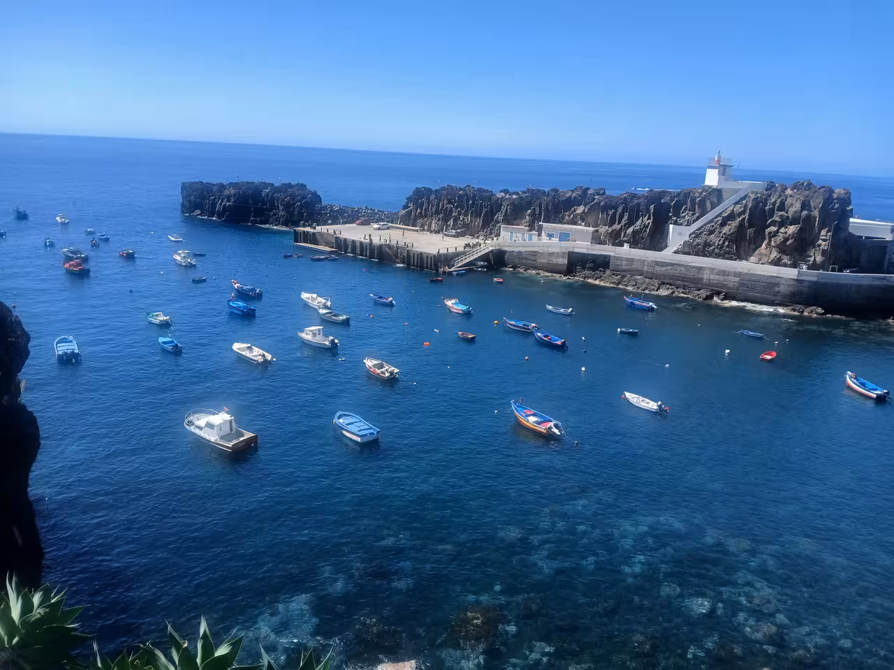 Colorful boats float in the clear blue waters of a scenic harbor on the Wine Route, Madeira.