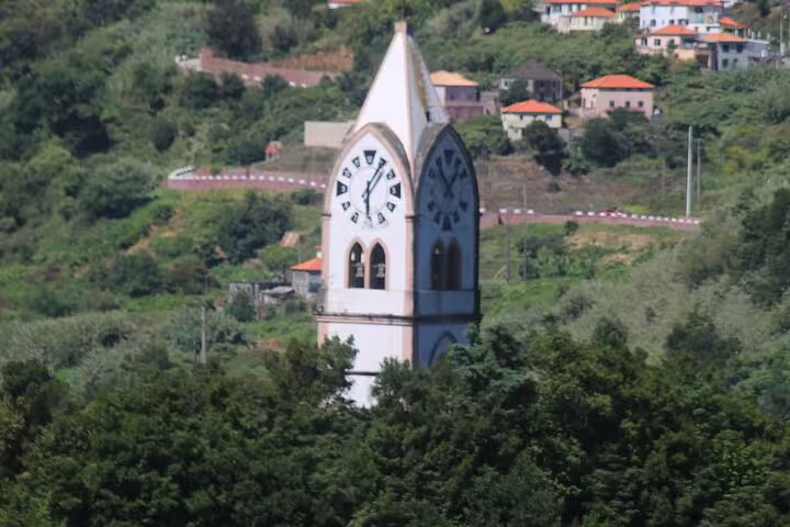 Scenic view of a historic clock tower amidst lush greenery on the Wine Taste 4x4 Jeep Adventure and Cabo Girão Skywalk tour.