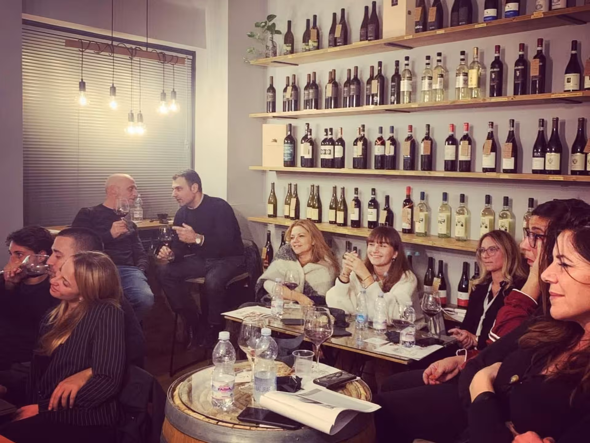 Group enjoying a lively wine tasting event in Naples, surrounded by shelves filled with various wine bottles.