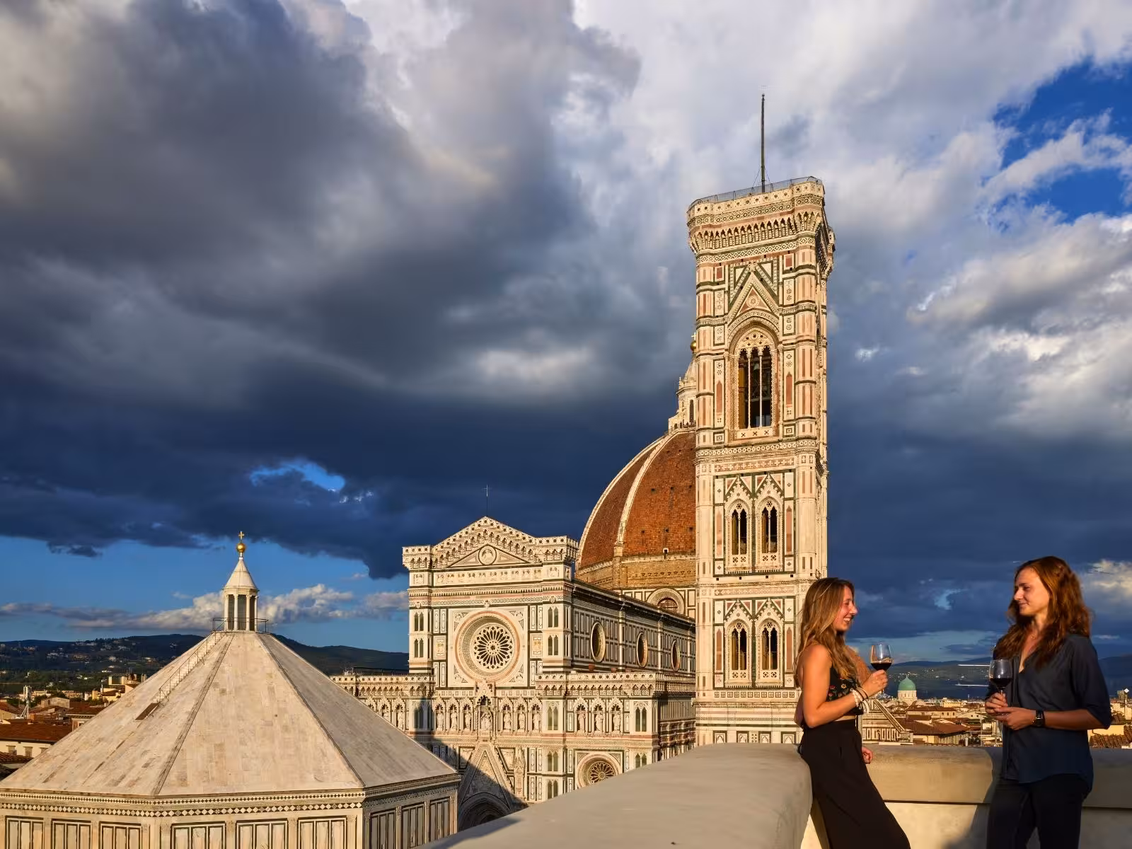 Two women enjoying wine on a Florence rooftop with a breathtaking view of the historic cathedral and skyline.