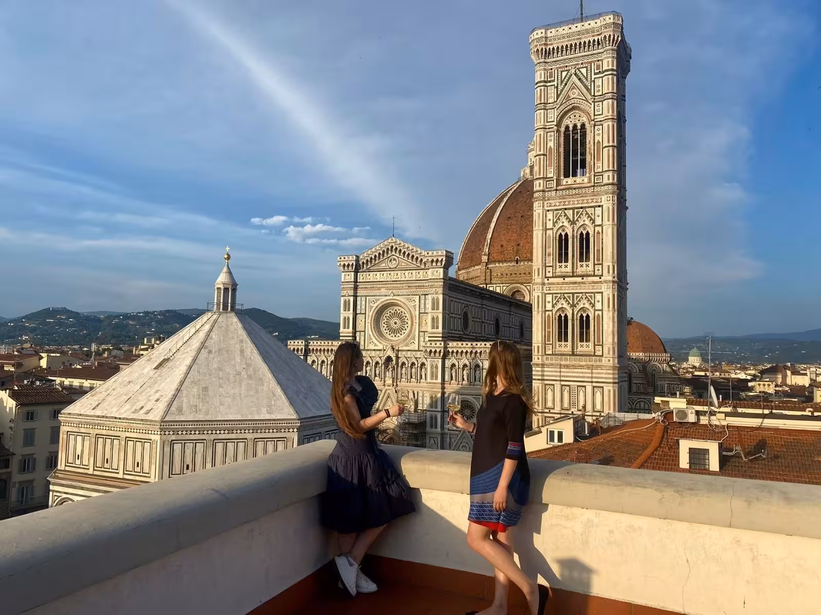Two women savoring wine on Florence rooftop with breathtaking Duomo and cityscape views.
