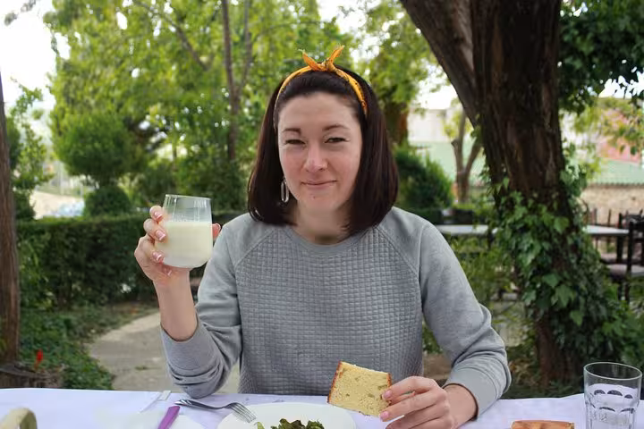 Woman enjoying local food and drink during a wine tasting and food tour in the lush surroundings of Berat, Albania.