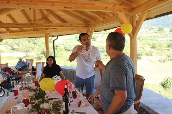 Guests enjoy a lively wine tasting and food tour under a wooden pavilion in scenic Berat, surrounded by nature.