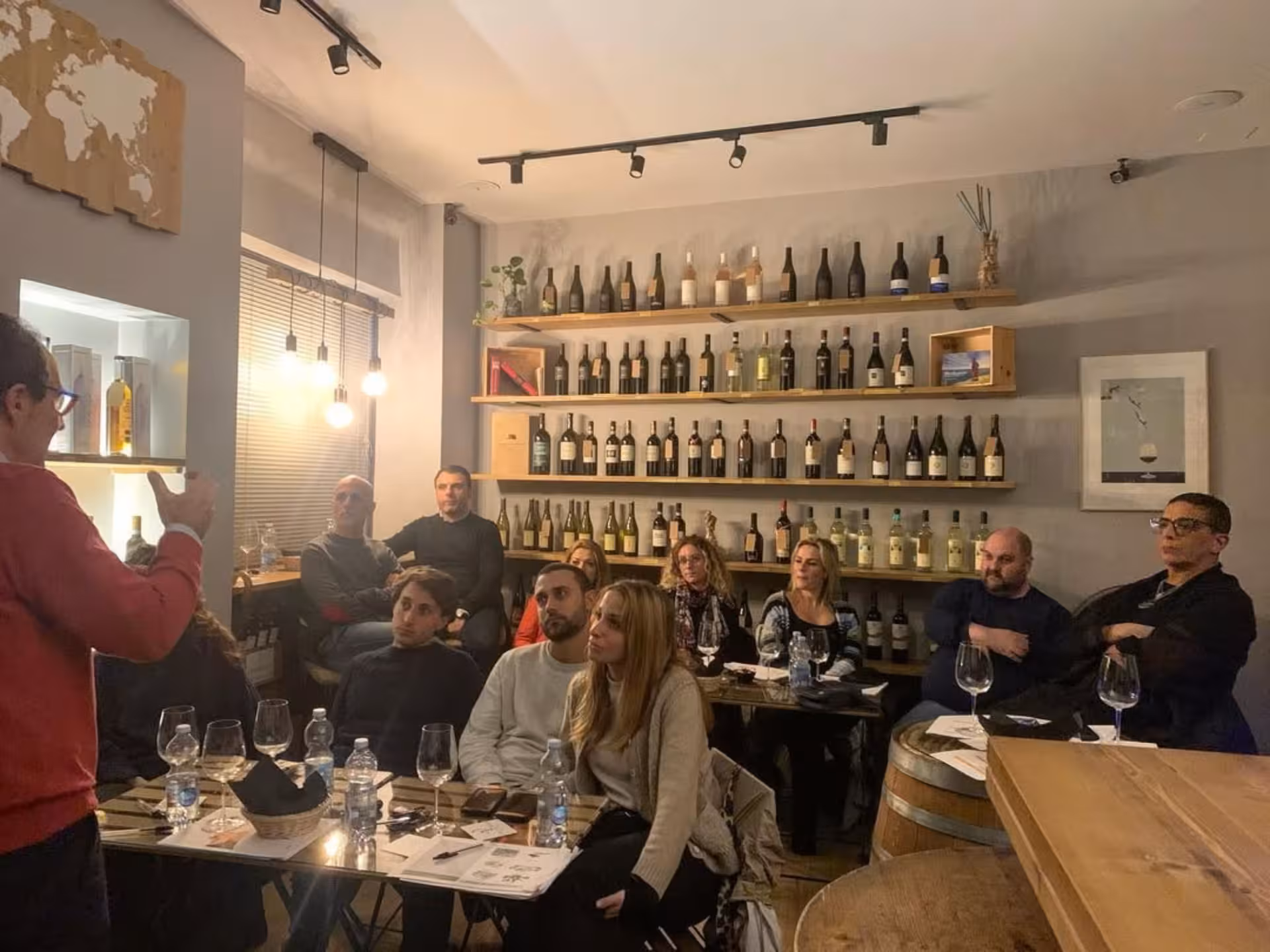 Group of people attentively listening to a wine expert in a cozy Naples wine bar setting.