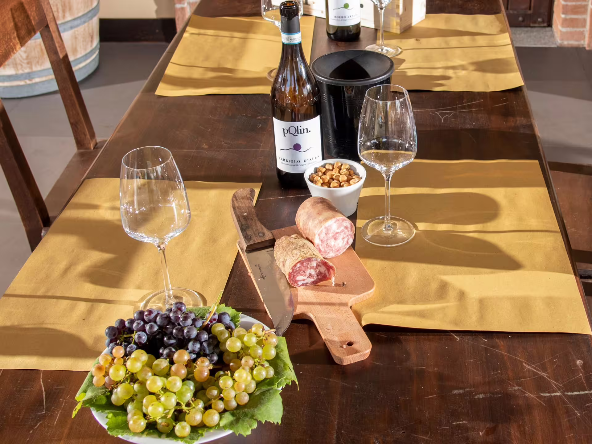 Indulge in wine tasting with Nebbiolo d'Alba, salami, and fresh grapes on a set dining table in Langhe.