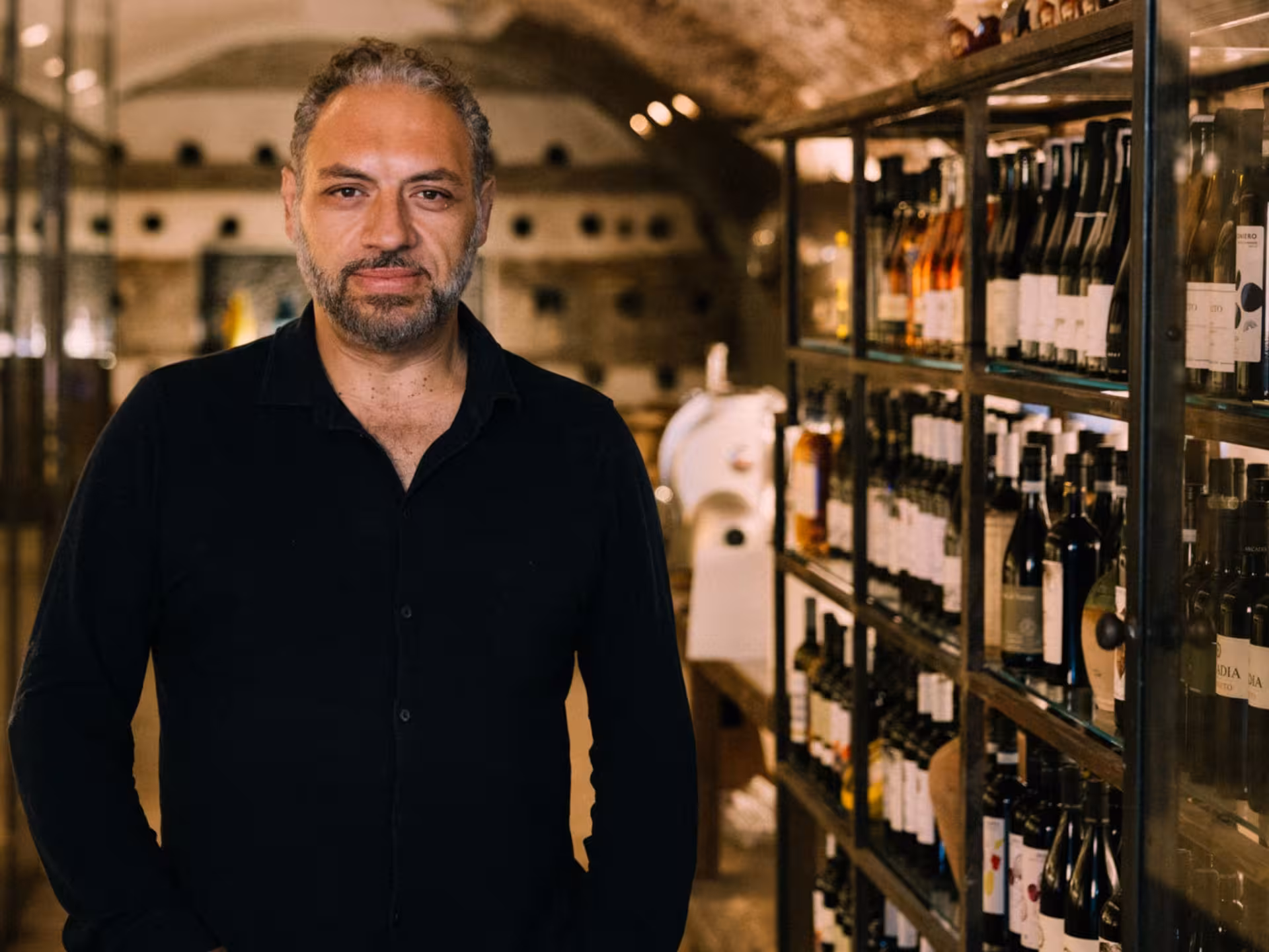 Man standing confidently beside wine racks in a dimly lit underground cellar in Rome, showcasing a wine tasting tour.