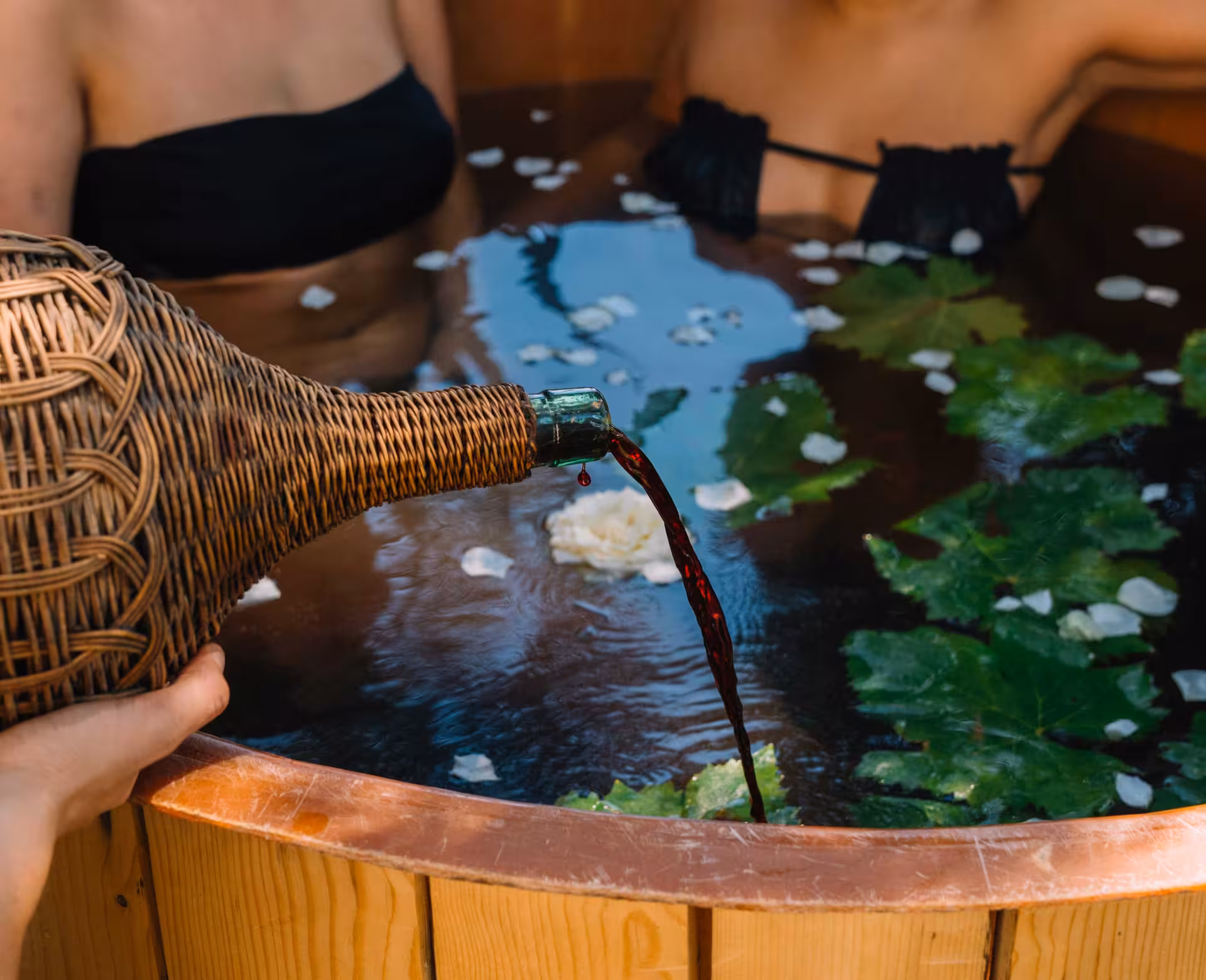 Wine being poured into a flower-filled wooden tub for a unique wine therapy experience in Gallura, Olbia.