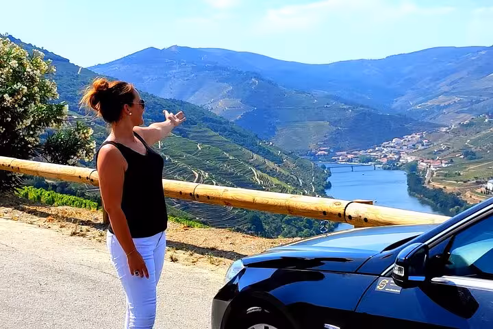 Wine trip viewpoint stop above terraced vineyards and river valley, traveler pointing out scenic Douro landscape