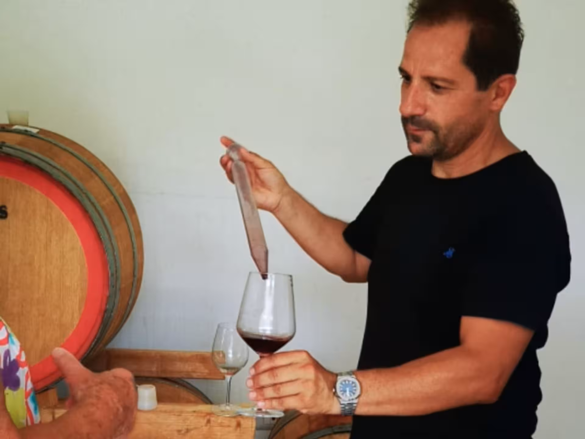 Winemaker pouring red wine from a barrel into a glass during a tasting session near Cagliari.