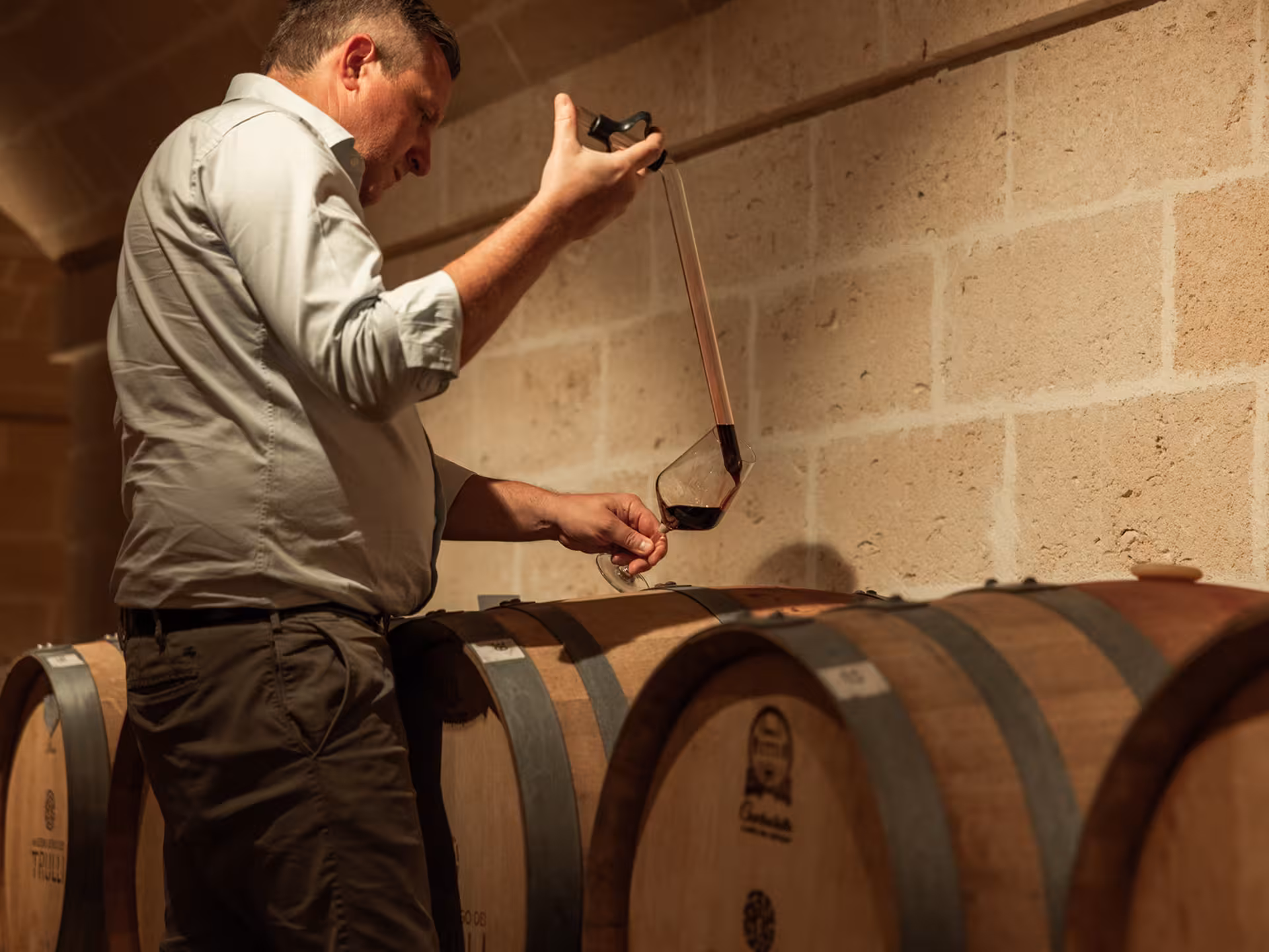 Winemaker sampling red wine from barrels at a Masseria winery near Taranto, Italy, showcasing traditional techniques.