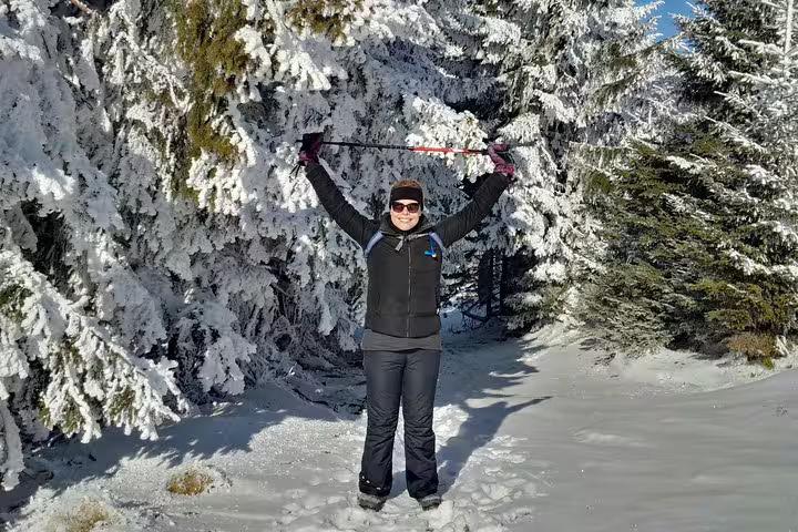 Hiker celebrating with arms raised on snowy trail surrounded by frost-covered pine trees in Piatra Craiului