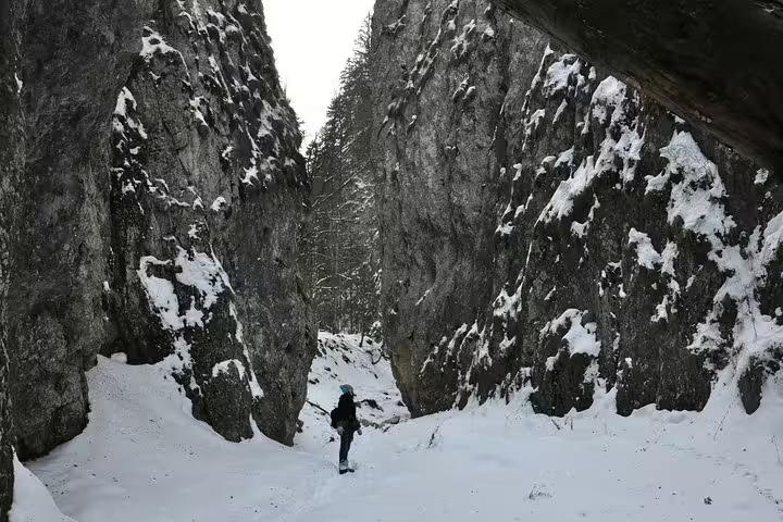Hiker walking through a narrow snow-covered rocky gorge in Piatra Craiului National Park in winter