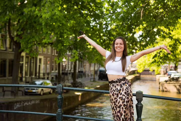 Woman joyfully posing on a scenic Amsterdam canal bridge, surrounded by lush trees, highlighting the vibrant Amstagram Tour experience.
