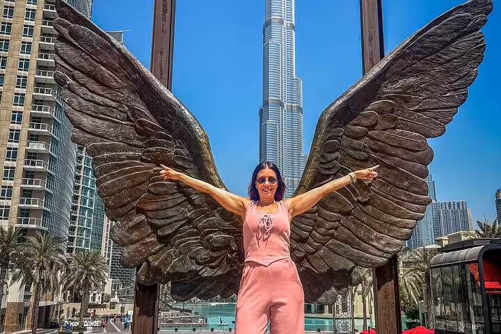 Woman posing with angel wings sculpture in front of Burj Khalifa, ideal for Instagram during a guided tour.