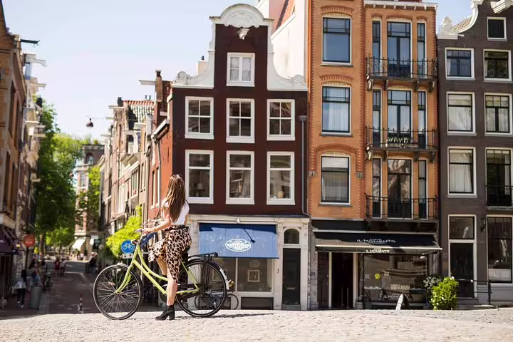 A woman with a bicycle enjoys a scenic view of Amsterdam's historic architecture during the Amstagram Tour & Moco Experience.